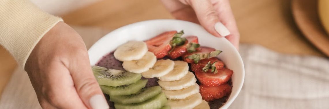 Delicious smoothie bowl topped with fresh fruits like kiwi, banana, and strawberries, held by manicured hands.