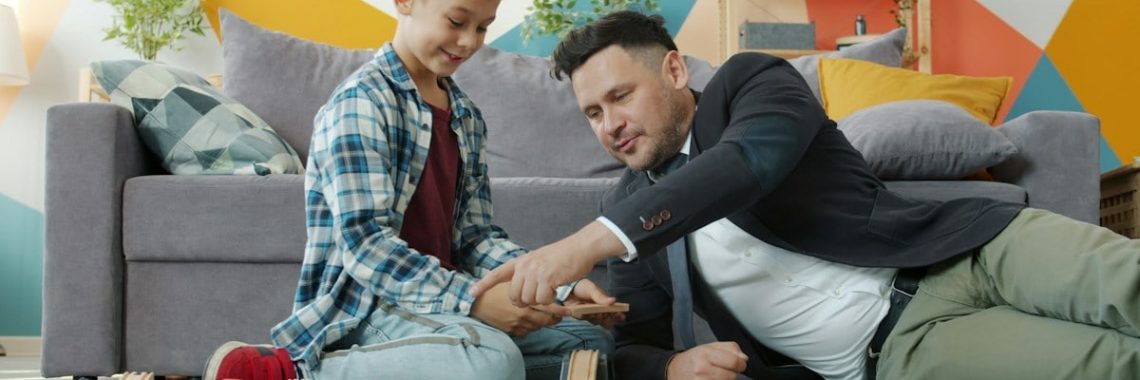 Dad businessman is playing with adorable little son holding toys relaxing in leisure time in house. Business people, family life and indoor activities concept.